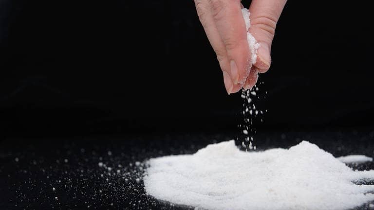 Hand die eine Prise Salz auf eine schwarze Flaeche streut  (Foto: Adobe Stock / yuryastankov)