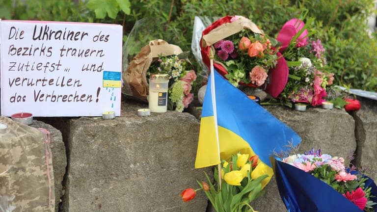 Am Gelände eines Einkaufszentrums in Murnau, an dem am Samstagabend (27.04.2024) zwei Männer aus der Ukraine getötet worden sind, wurden Blumen niedergelegt, sowie eine kleine ukrainische Flagge aufgestellt. Die Polizei konnte einen Mann festnehmen, der als dringend tatverdächtig gilt. Es handelt sich dabei um einen 57 Jahre alten Russen. (Foto: dpa Bildfunk, picture alliance/dpa | Constanze Wilz)